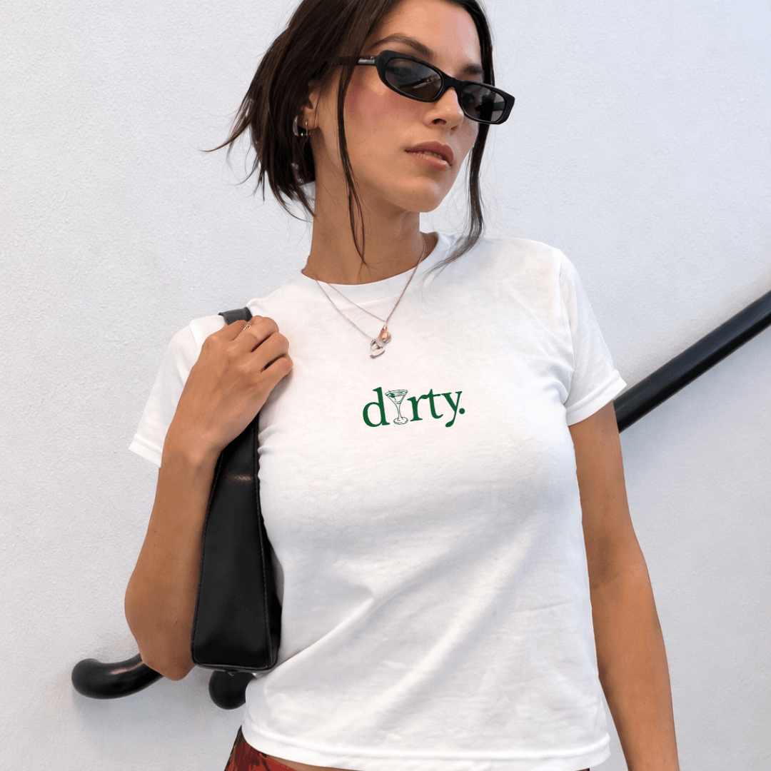 Woman wearing a white t-shirt with 'dirty.' text, holding a black bag against a light gray background