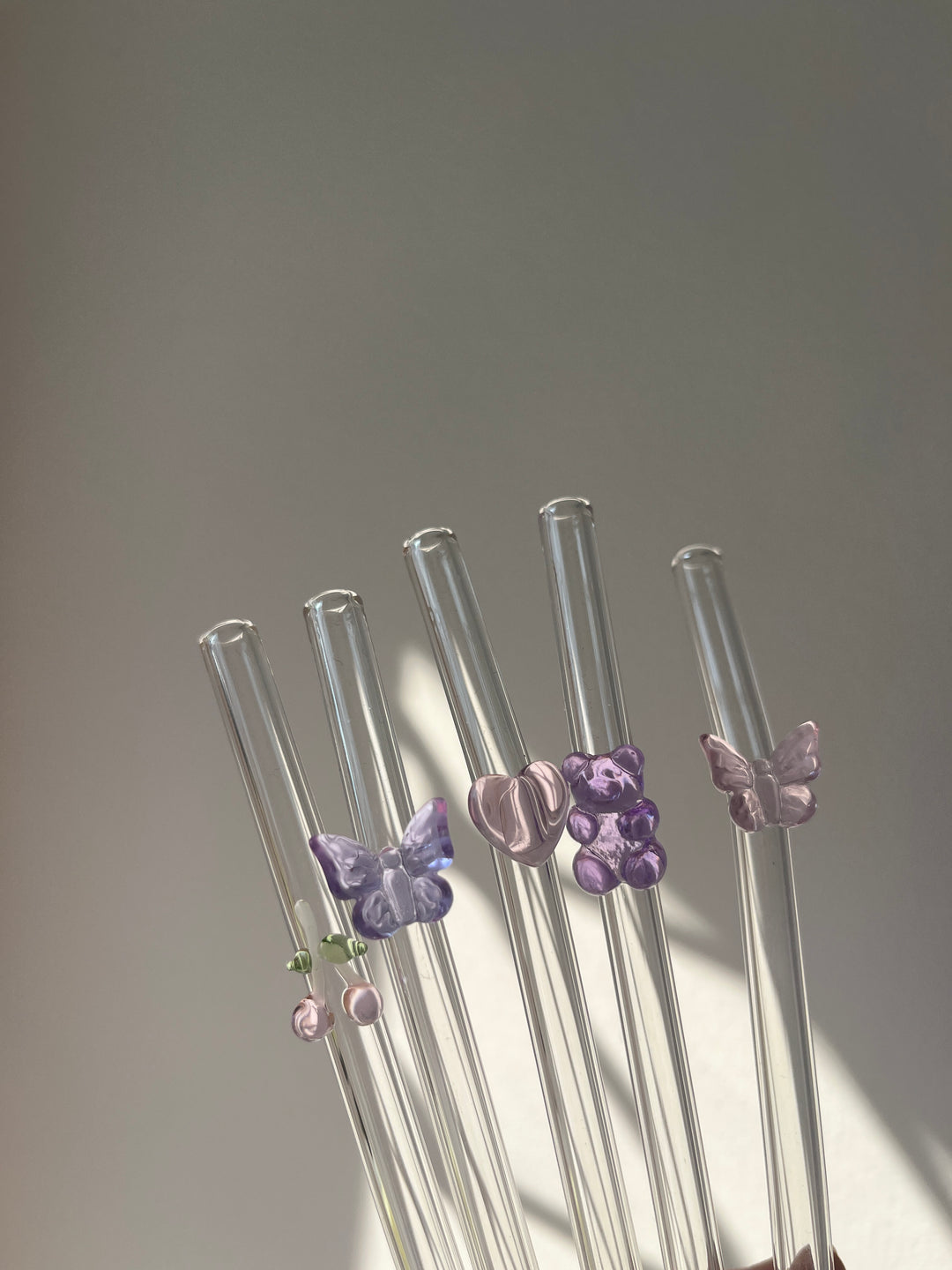 Set of glass straws with decorative butterfly ends on a gray background