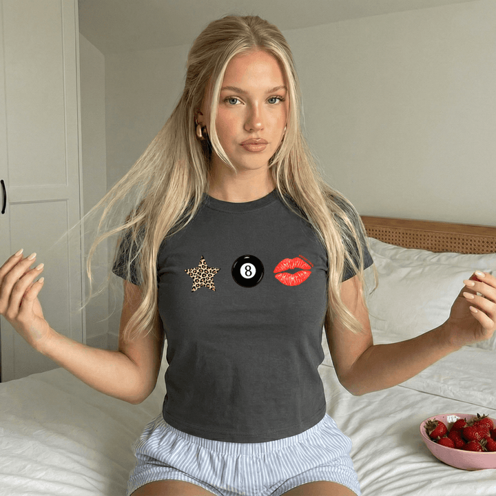 Woman wearing a dark gray t-shirt with a star, number 8, and lips design on a bed.