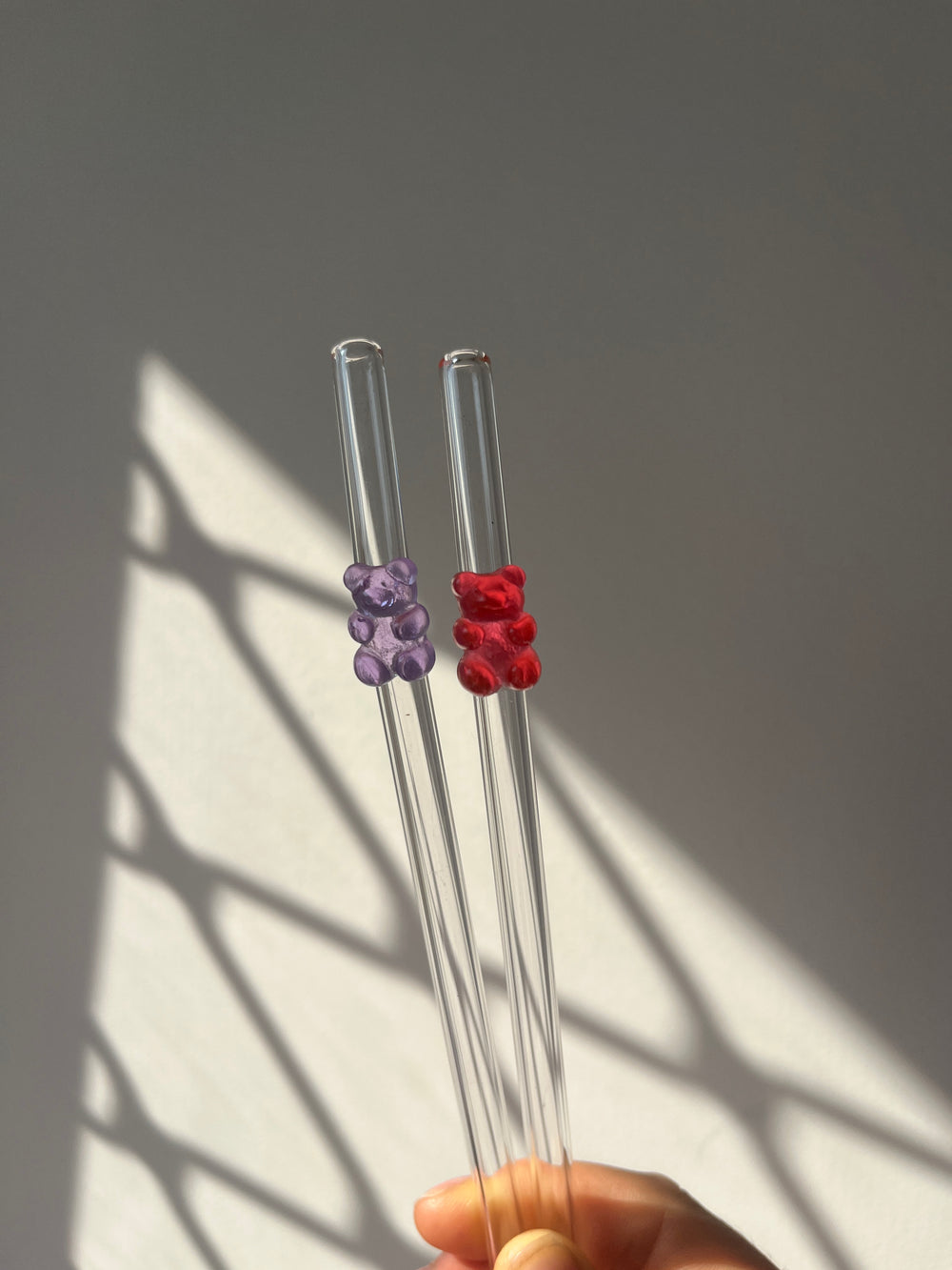 Clear glass straws with red and purple decorative ends held by a hand against a gray background