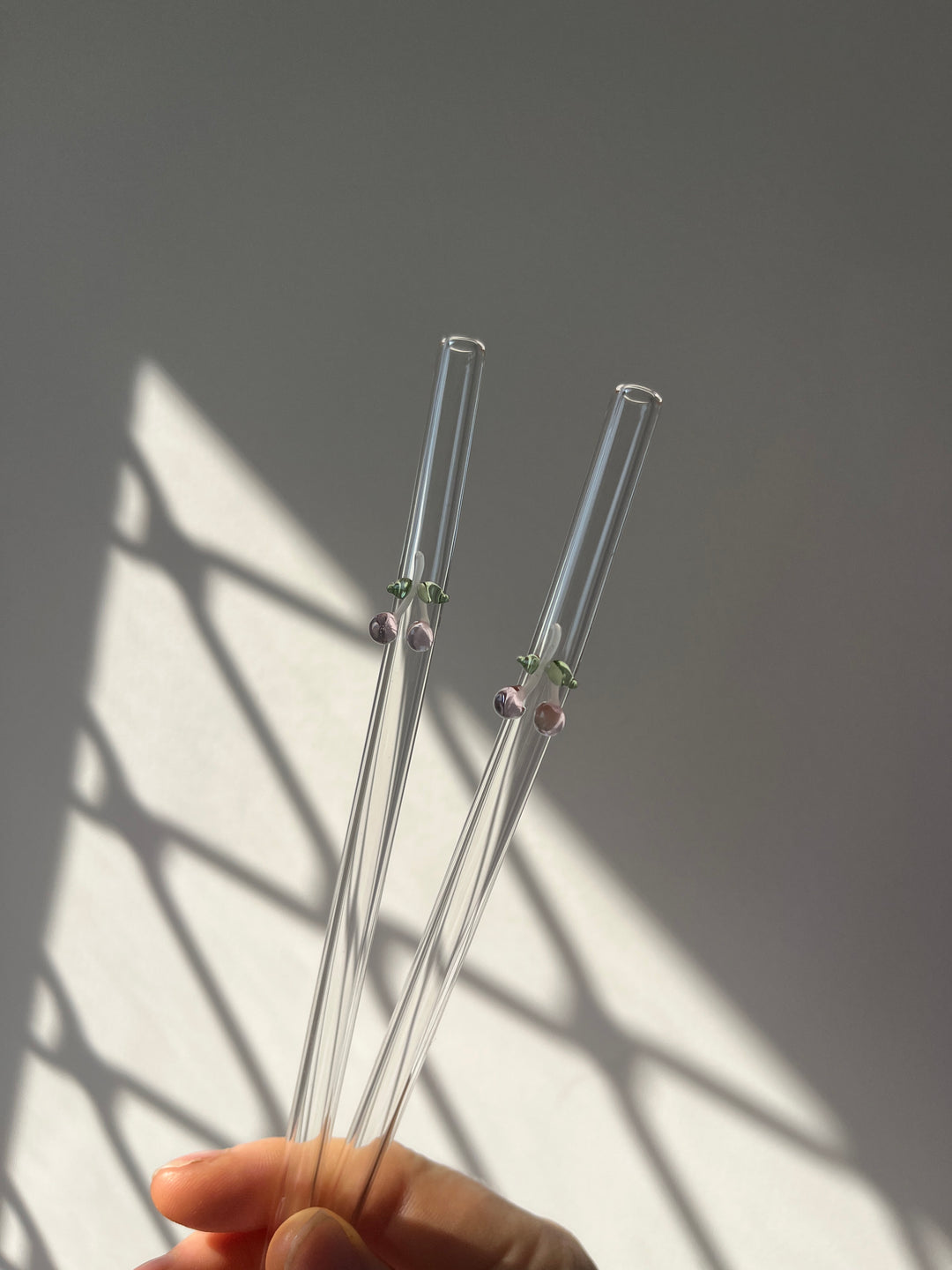 Clear glass straws held by a hand on a light background